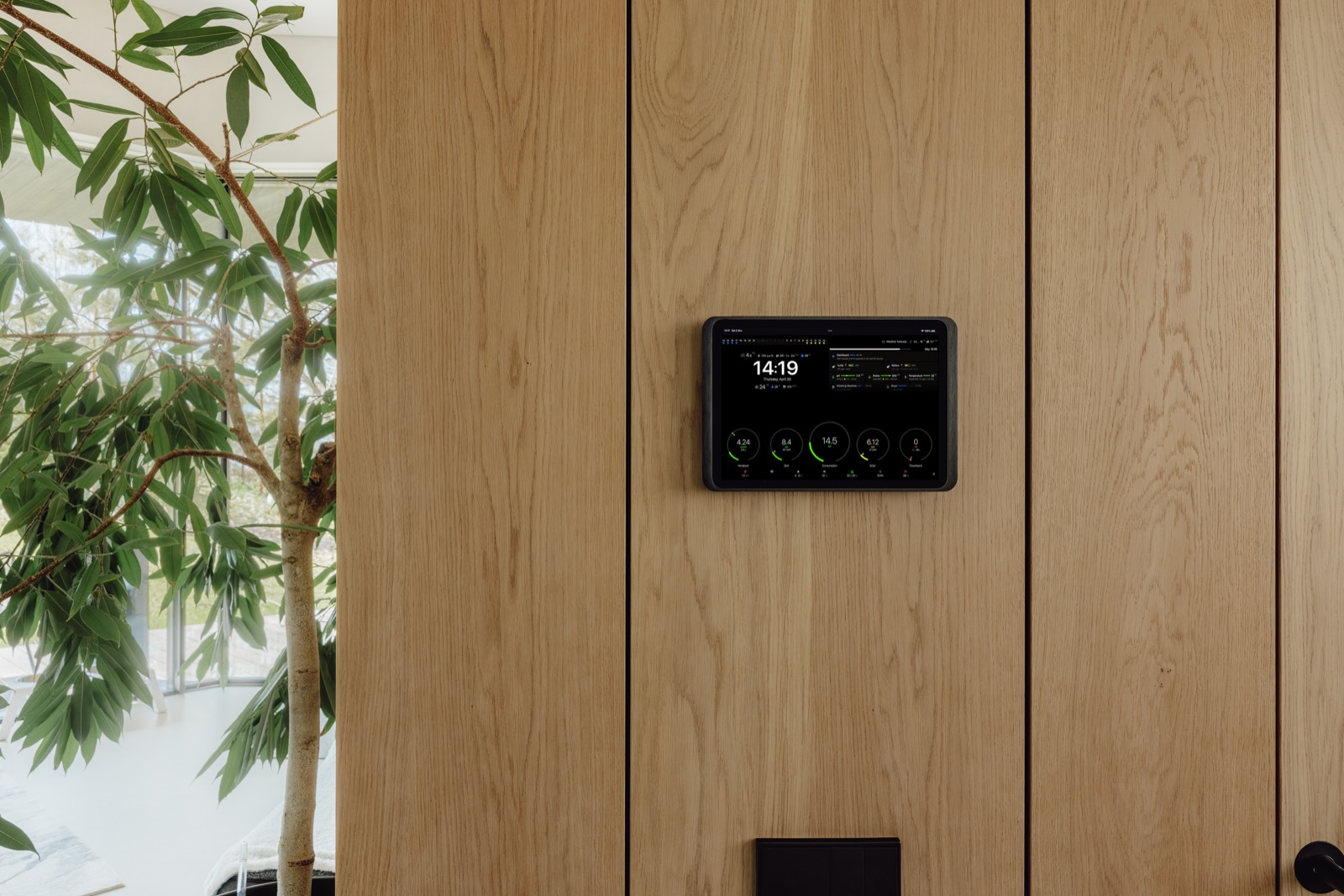 Wall-mounted control display flush-mounted on an oak panel beside a window