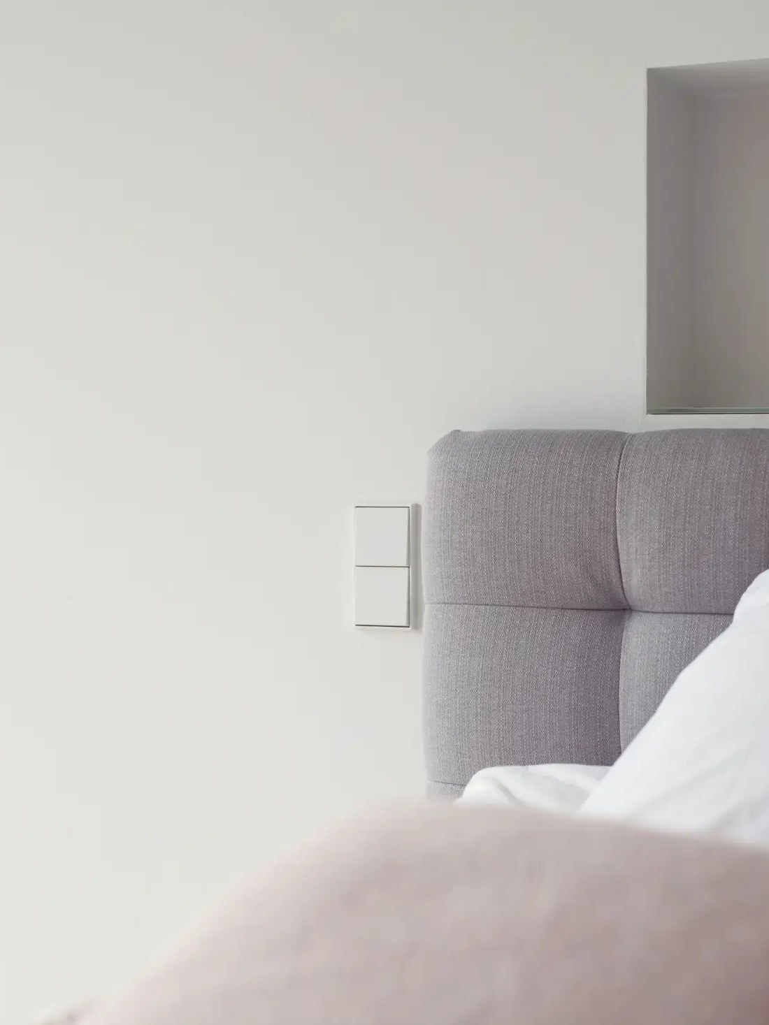 Jung LS 990 momentary push-button on a bedroom wall beside an upholstered headboard