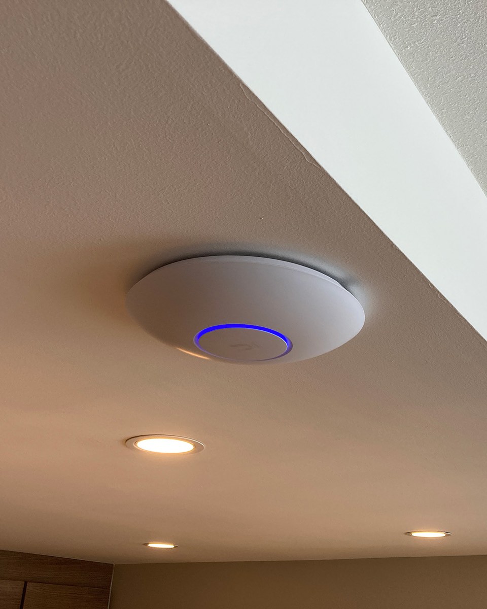 UniFi access point flush-mounted on a vaulted ceiling with its LED ring lit